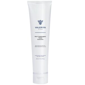 The image shows a tube of "Non-Comedogenic Tinted Sunscreen" from the brand Valeriya Life, featuring a sleek, white tube. The product label displays the name, key ingredients and benefits in a modern, clean font. The tube is placed against a light-colored background, emphasizing its minimalistic and practical design. The sunscreen has a tinted formula and is designed to protect the skin from harmful UV rays while providing a natural, even coverage. This sunscreen is ideal for those with sensitive or acne-prone skin, offering sun protection without clogging pores.